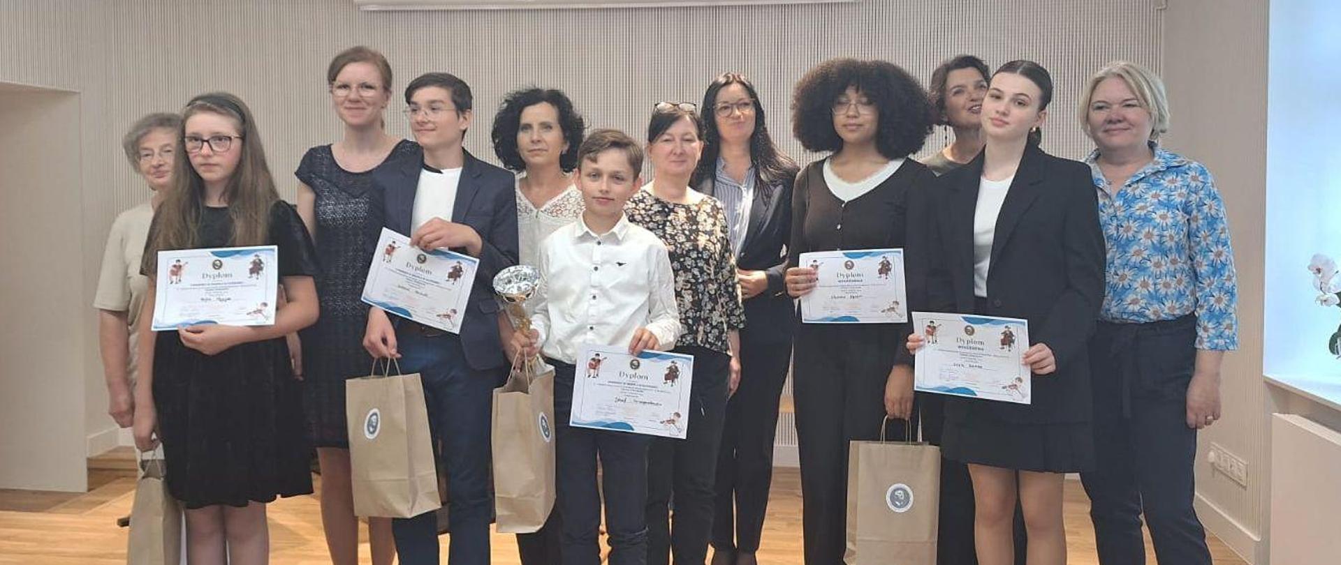 Uczestnicy konkursu stoją pozując do zdjęcia. Dzieci trzymają dyplomy i torby z upominkami.