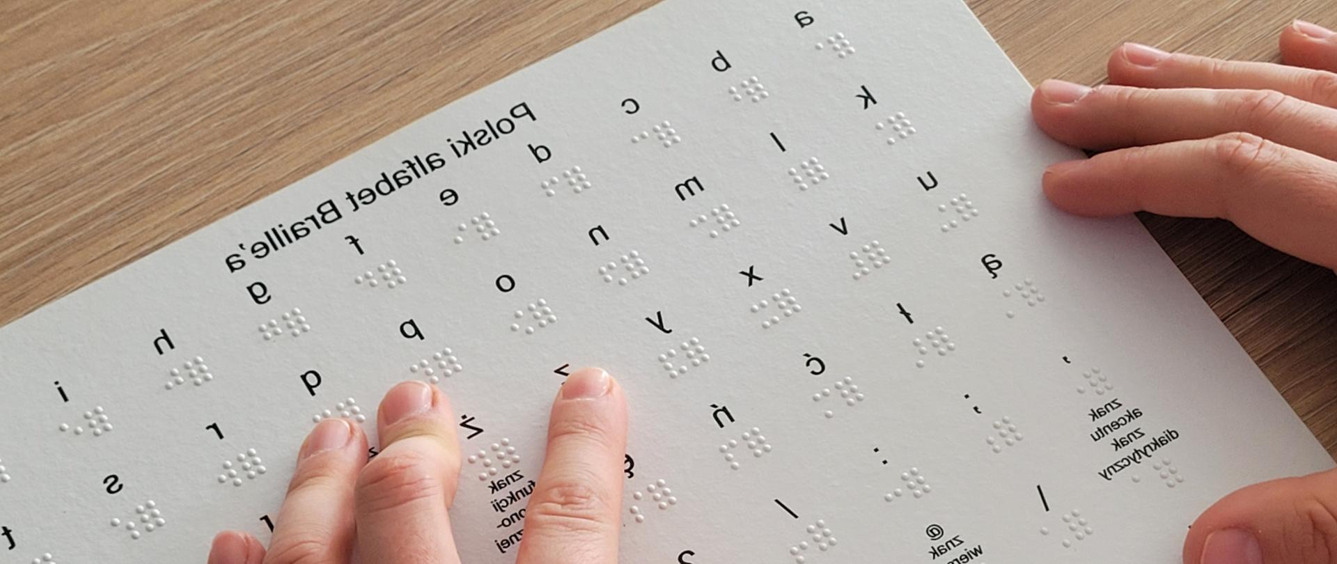 Alfabet Braille’a wydrukowany na sztywnym kartonie oraz dłonie osoby, która zapoznaje się
z techniką czytania i rozróżniania liter.
