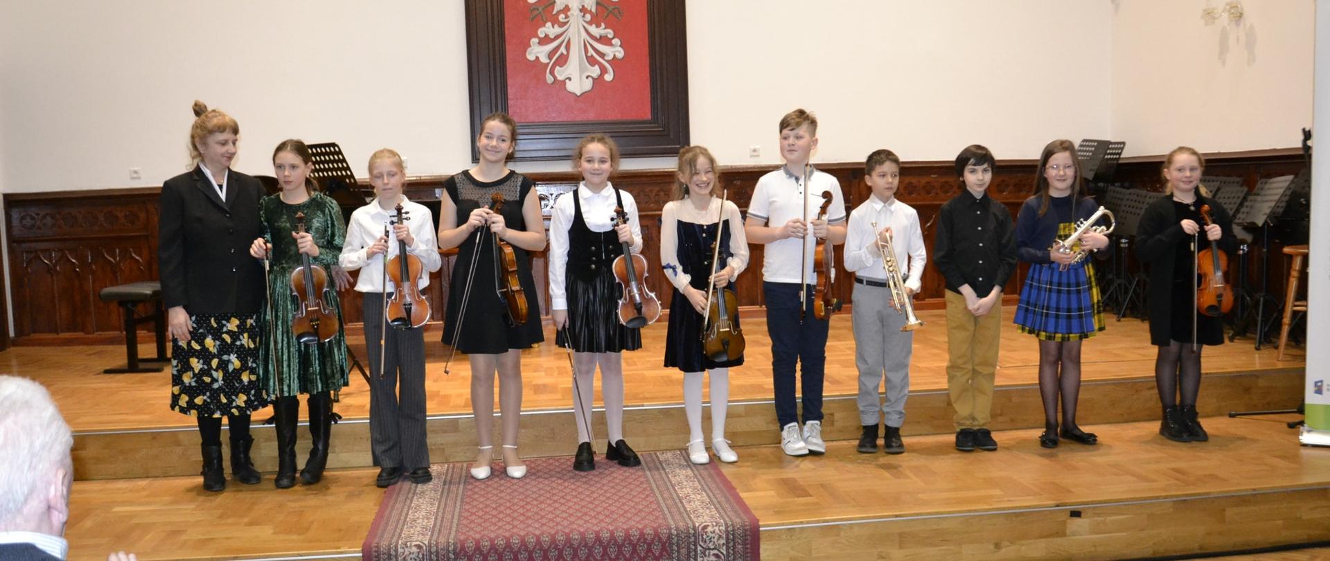 uczniowie klasy 3B cyklu 6-letniego na koncercie klasowym, stojący na scenie w Sali Królewskiej PSM Mielec