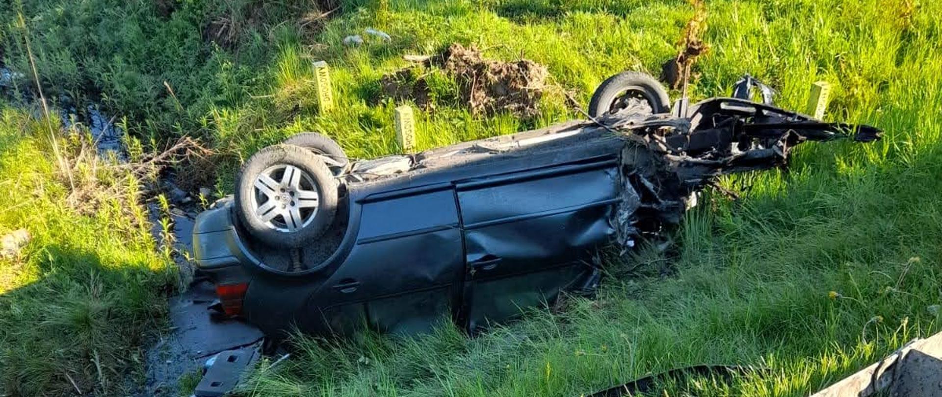 Samochód osobowy leżący na dachu poza jezdnią