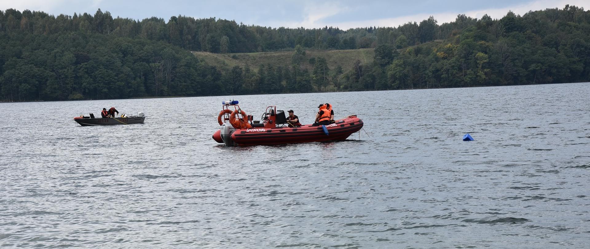 Zdjęcie obrazuje akwen z 2 łodziami i strażakami na pokładzie w tle drzewa 
