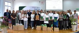 Grupa uczestników, opiekunów i jurorów w strojach kucharskich i formalnych pozuje na scenie podczas gali V Ogólnopolskiego Konkursu Gastronomicznego „SLOW FOOD 2026”.