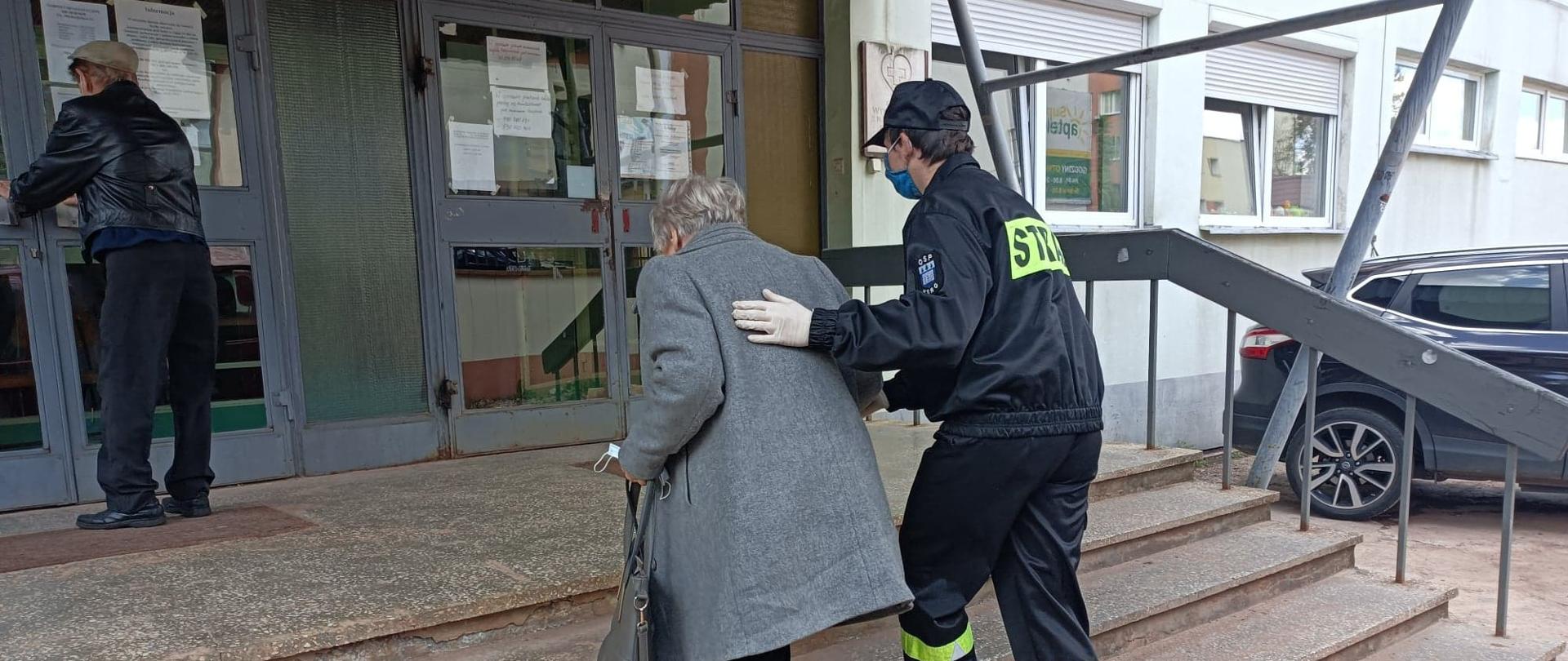 Strażak odprowadza osobę do punktu szczepień