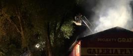 Na zdjęciu widać działania gaśnicze strażacy podają wodę z drabiny mechanicznej na płonący dach budynku