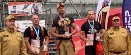 Zdjęcie przedstawia na podium trzech strazków oraz dwóch co im wręczaja nagrody.