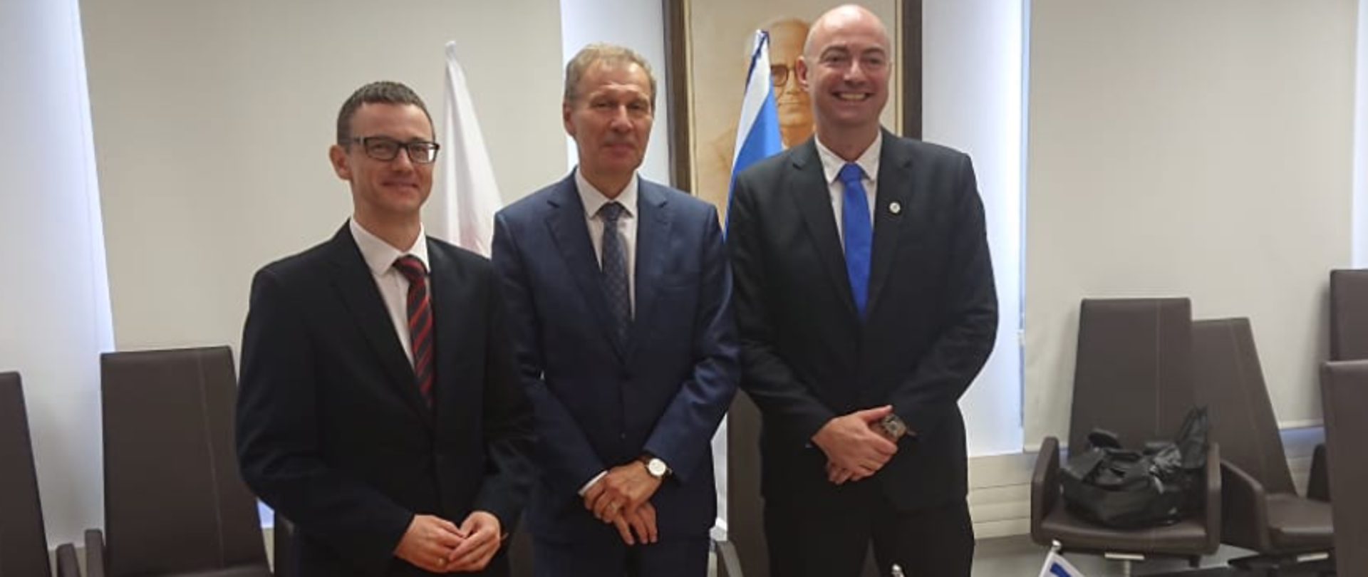 Minister Karol Okoński, dyrektor Krzysztof Silicki oraz Yigal Unna stoją za stołem. Na stole notatki i flagi.