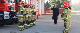 Strażacy z Jednostki Ratowniczo-Gaśniczej w Bielsku Podlaskim oddają hołd poległym strażakom z Ukrainy. Strażacy ustawieni są na tle samochodów ratowniczo-gaśniczych. Prowadzący oraz dowódcy zmian służbowych oddają honory.