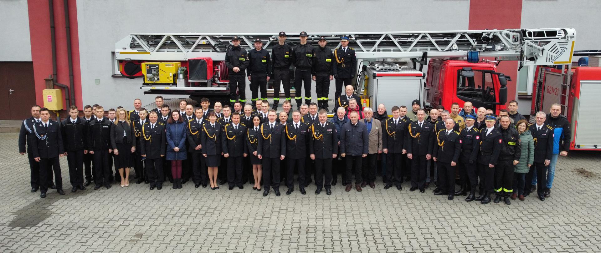 Zdjęcie przedstawia wszystkich zebranych gości, strażaków i pracowników cywilnych. Za nimi ustawiona drabina strażacka.