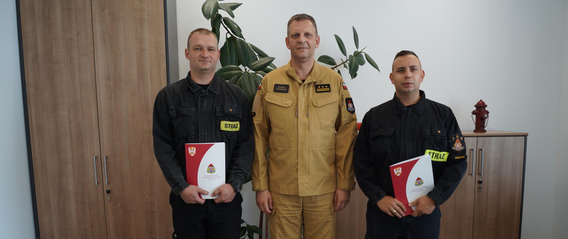 Zdjęcie przedstawia trzech strażaków stojących w biurze