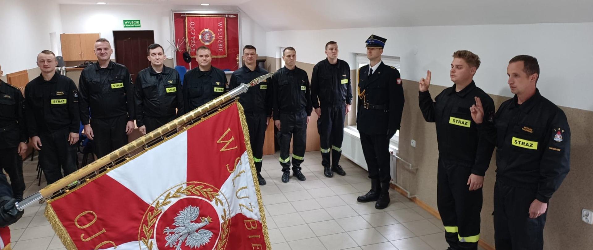 Ślubowanie nowo przyjętych strażaków KP PSP Radziejów. Strażacy składają ślubowanie na sztandar KP PSP Radziejów. W tle stoi pododdział strażaków.