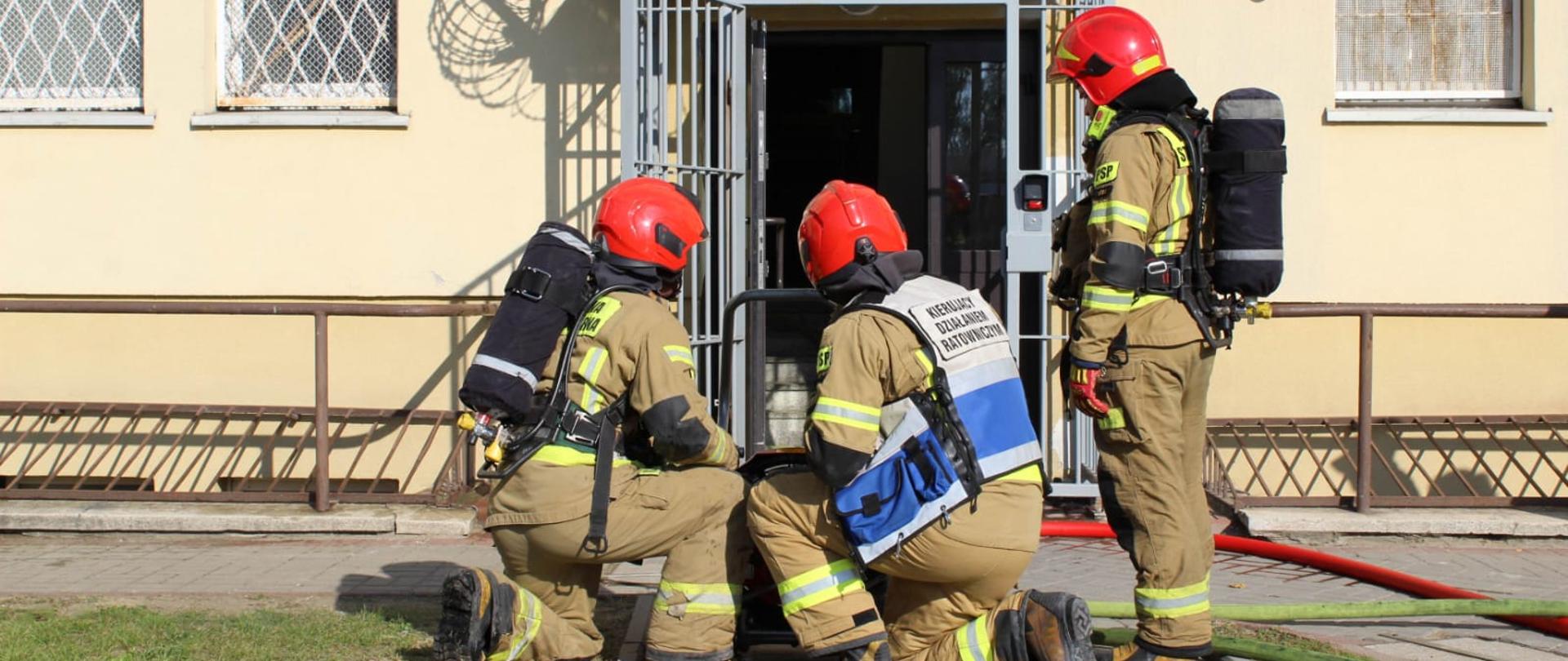 Strażacy w ubraniach specjalnych i aparatach ochrony układu oddechowego przed wejściem do aresztu