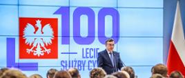 Wystąpienie szefa służby cywilnej Dobrosława Dowiata-Urbańskiego - w tle ekran z logo 100-lecia służby cywilnej i flaga Polski