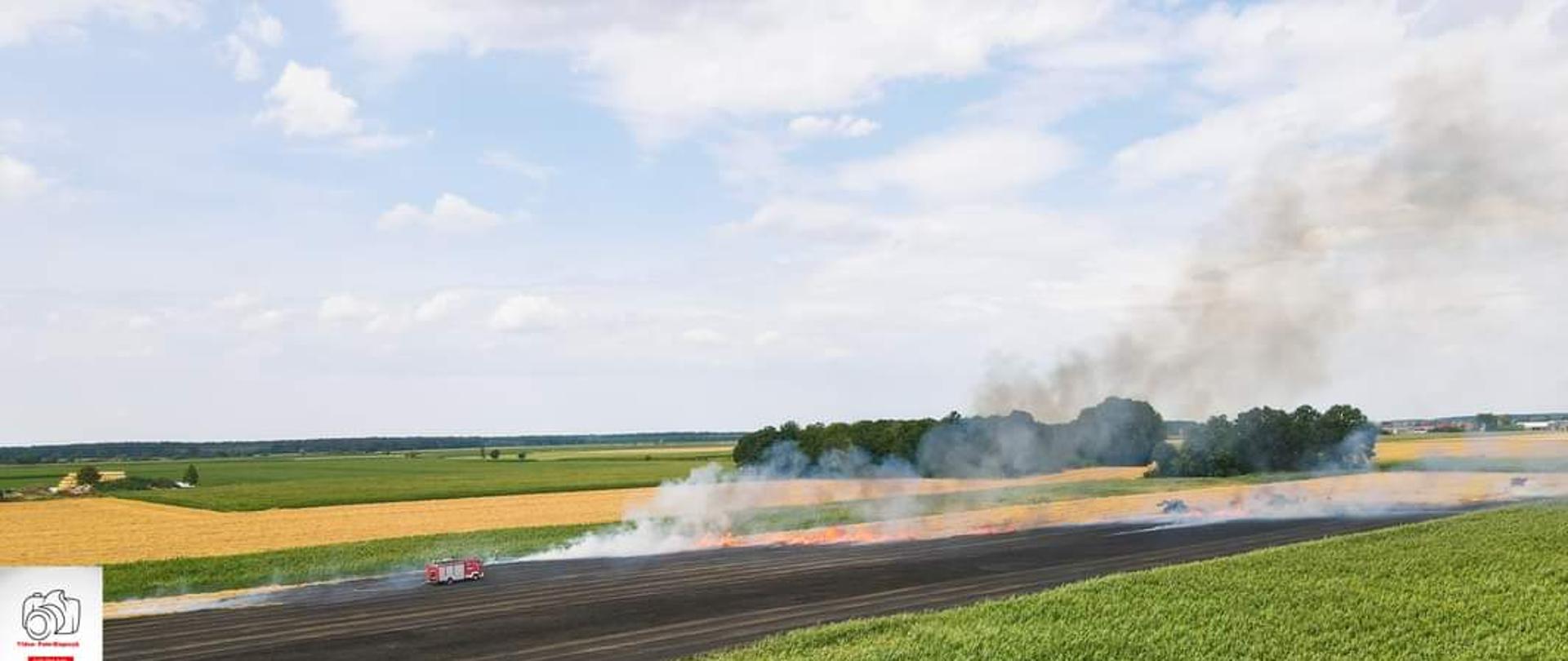 Pali się śceirnisko oraz zboże. Front pożaru zgodnie z kierunkiem wiatru trawi kolejne metry. Występuje duże zadymienie. Rolnicy sprzętem rolniczym wykonują pasy ochronne ograniczające rozprzestrzenianie się ognia. Strażacy pojazdem pożarniczym poruszają się po powierzchni spalonej dogaszając zarzewia. 