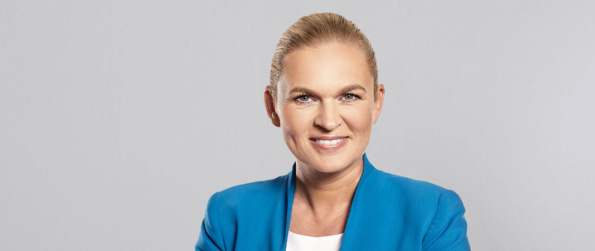 Minister Barbara Nowacka w niebieskiej marynarce na jasnoszarym tle.