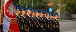 Strażacy w mundurach wyjściowych stoją w szeregu.