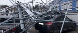 Zdjęcie przedstawia pojazdy przygniecione instalacją fotowoltaiczną zerwaną z dachu przez porywisty wiatr
