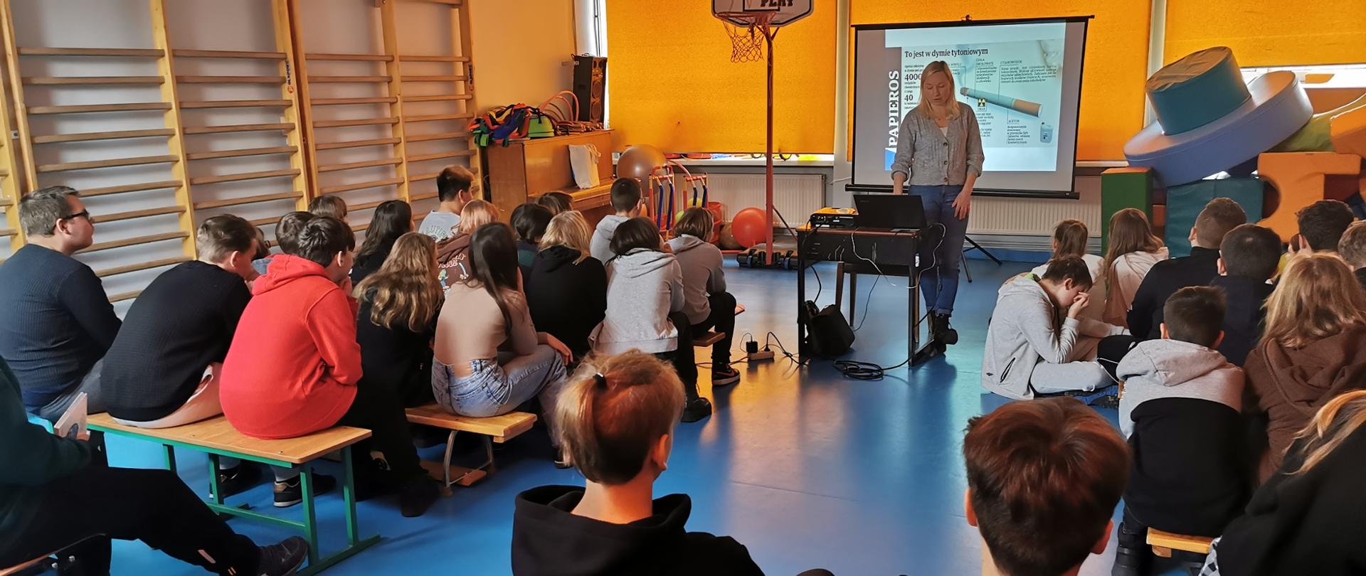 Uczniowie zgromadzeni na sali słuchają prelekcji
