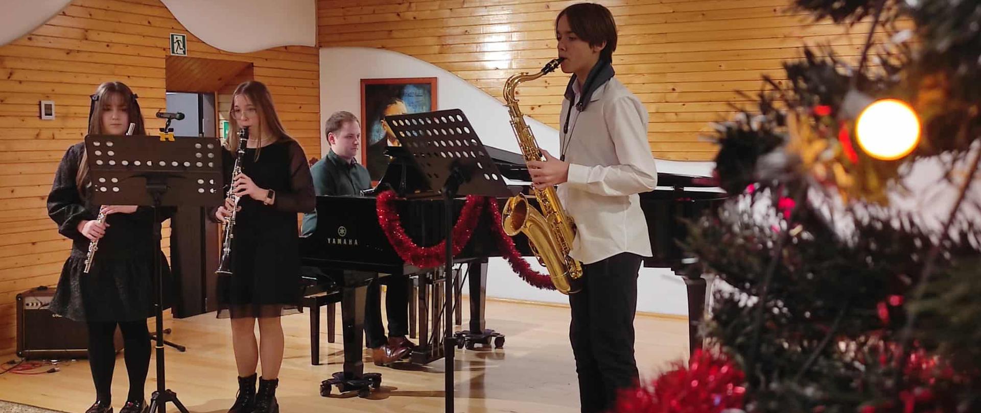 uczniowie grający na instrumentach dętych drewnianych z akompaniamentem na fortepianie