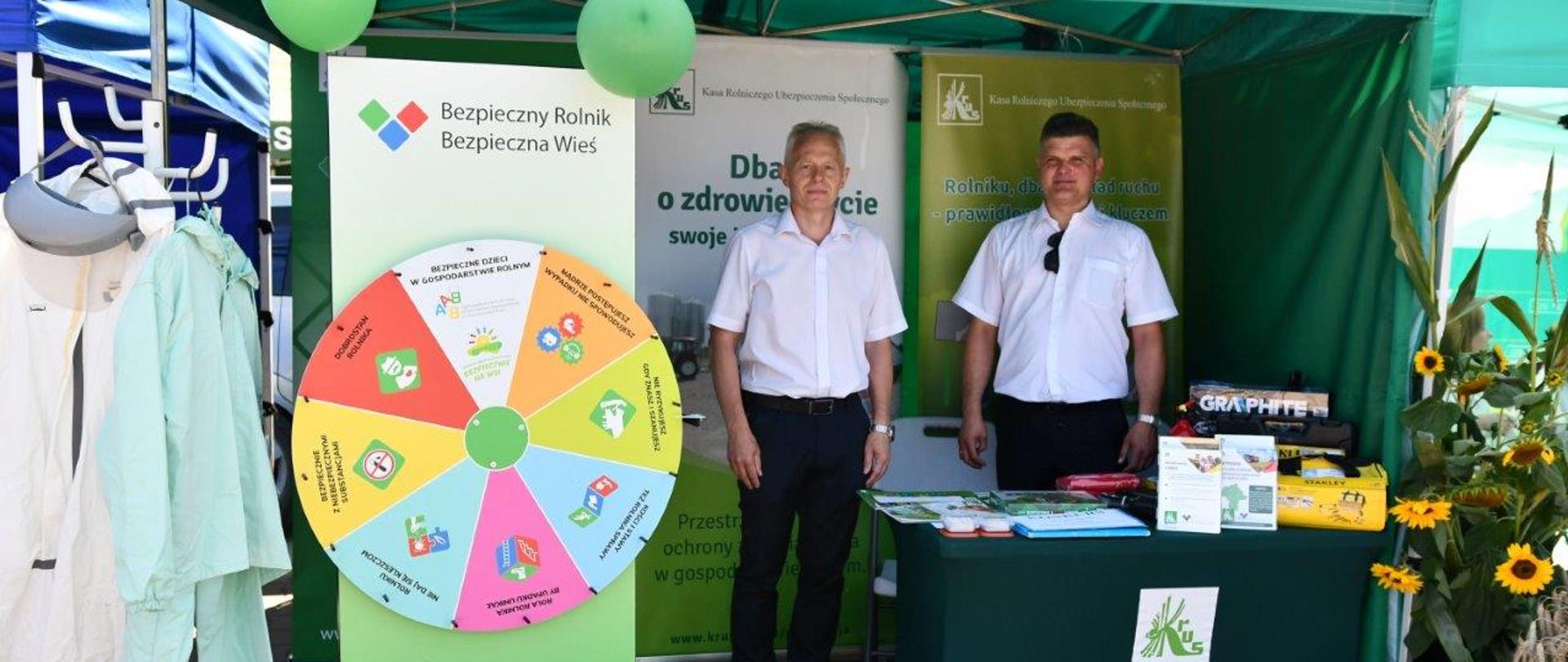 Stoisko informacyjno-prewencyjne Kasy wraz z wyposażeniem, wewnątrz stoiska mężczyzna stoi dwóch mężczyzn.