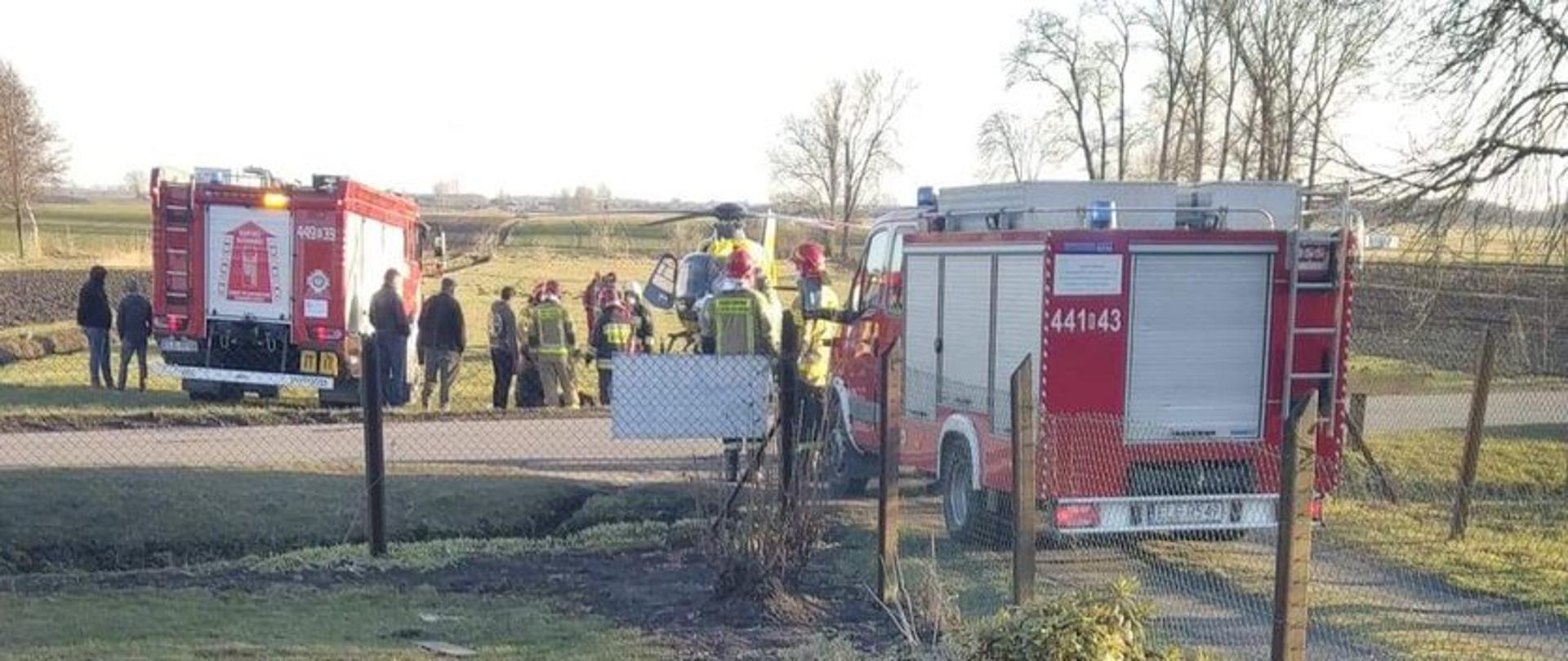 Na zdjęciu widać samochody strażackie, strażaków, śmigłowiec Lotniczego Pogotowia Ratunkowego oraz osoby postronne obserwujące działania ratownicze.