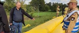 Dyrektor Piotr Kowalski wskazuje poprawne ułożenie rękawa przeciwpowodziowego
