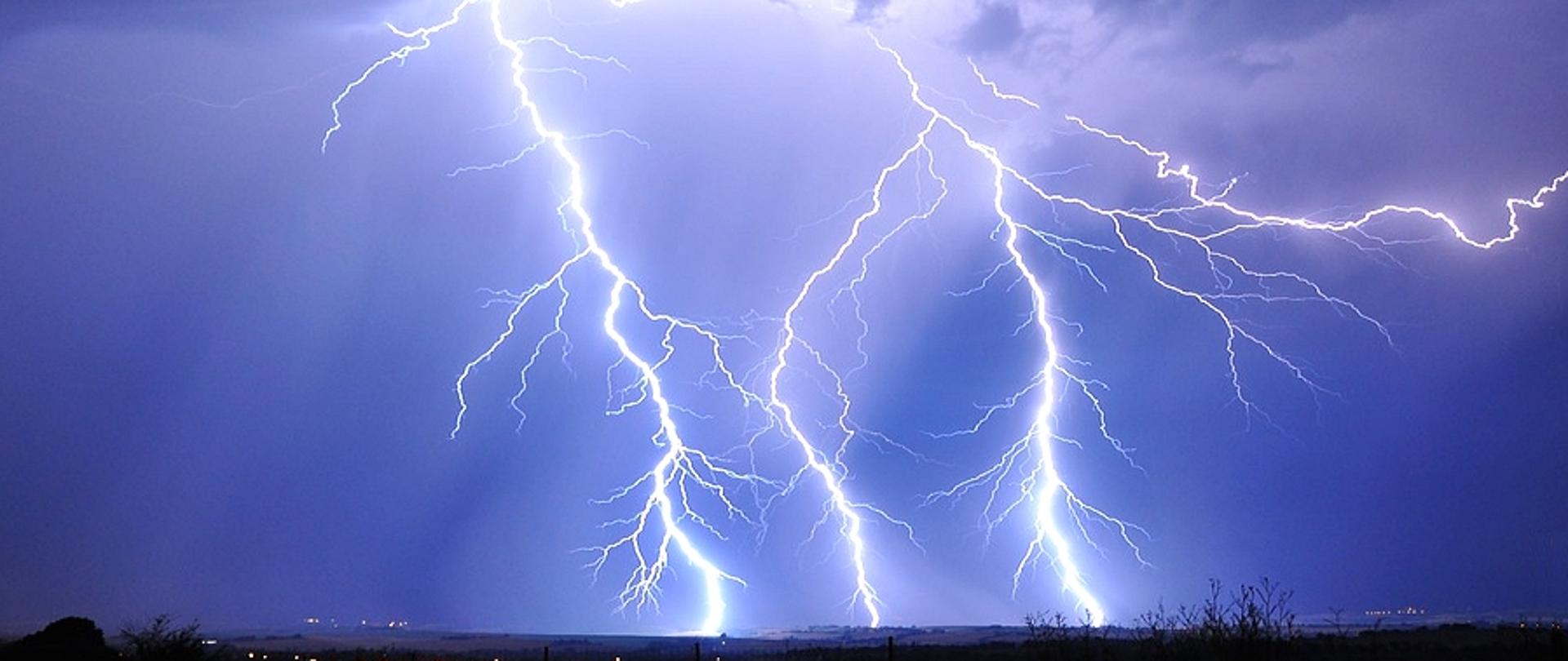 Niebo w kolorze ciemno niebieskim. Na jego tle uderzenie pioruna