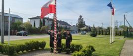 Strażacy wciągają flagę Polski na maszt podczas uroczystej zbiórki