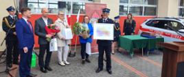 Zdjęcie przedstawia Komendanta Powiatowego i samorządowców z terenu powiatu z pamiątkową grafiką