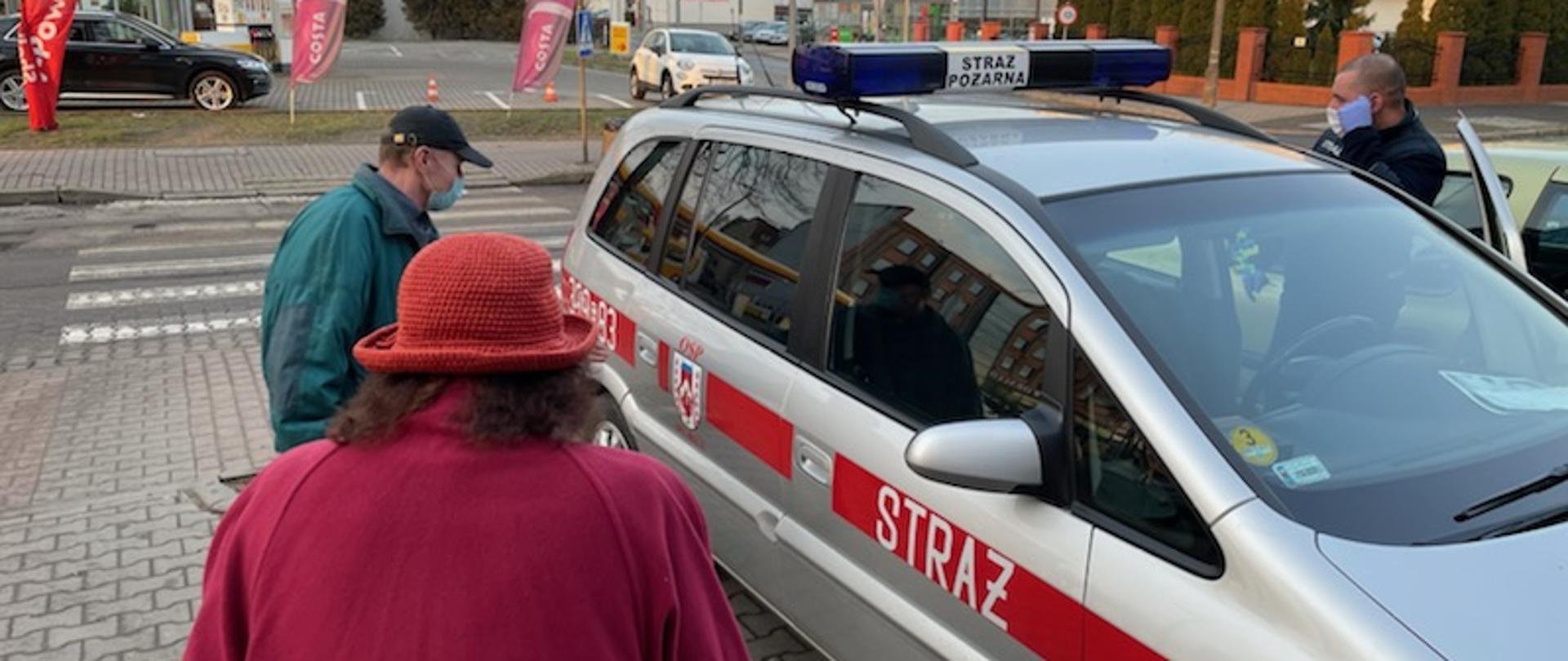 Samochód operacyjny jednostki OSP w Słubicach wraz z widocznym strażakiem OSP oraz dwiema osobami zmierzającymi do tego pojazdu.