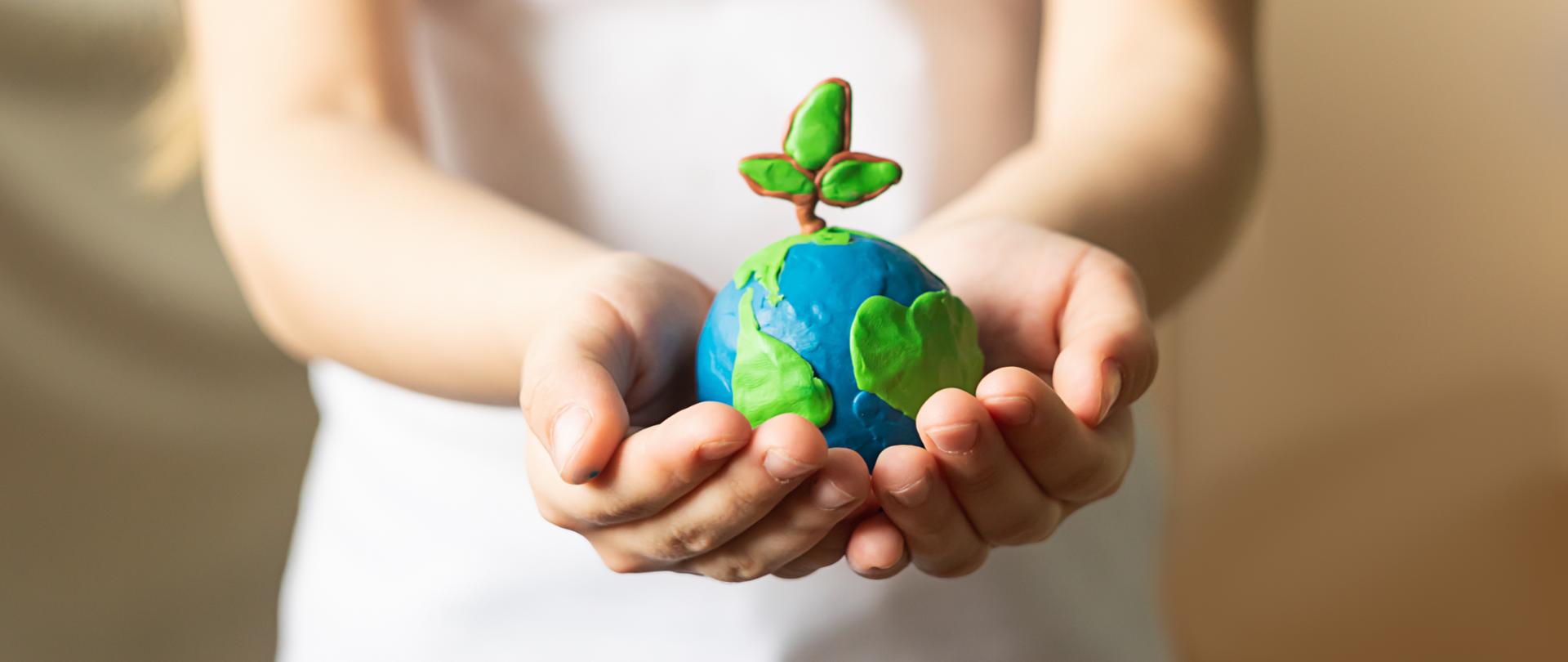 A small globe with trees in the hands of a child. Layout of the planet made of plasticine in children's palms. Concept ecology. Copy space. Horizontal frame.