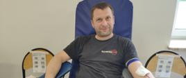Na zajęciu widoczny mężczyzna siedzący na fotelu na sali oddający krew podczas akcji zbiórki krwi zorganizowanej przez Klub Honorowych Dawców Krwi Polskiego Czerwonego Krzyża przy Komendzie Powiatowej Państwowej Straży Pożarnej w Gorlicach i Klub Honorowych Dawców Krwi Polskiego Czerwonego Krzyża Moszczenica.