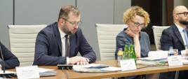 Minister Grzegorz Puda na posiedzeniu Komitetu Koordynującego ds. Polityki Rozwoju, minister siedzi przy stole i przemawia do mikrofonu
