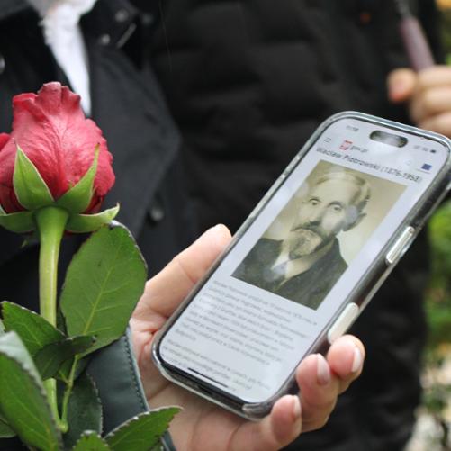 zdjęcie przedstawia zbliżenie na ekran telefonu wyświetlający informacje o zmarłym, widoczny kwiat róży