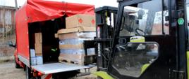 Operator wózka widłowego pakuje paletę ze środkami do dezynfekcji na przyczepę samochodu z Komendy Powiatowej Państwowej Straży Pożarnej w Pleszewie. 