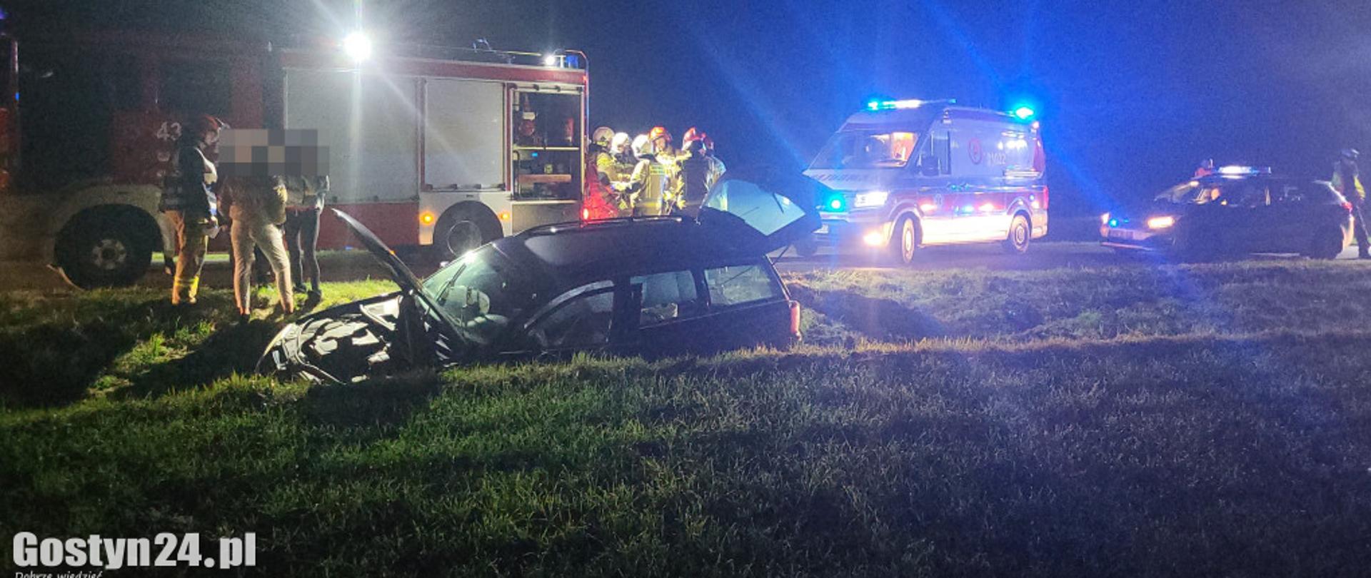 Wrak samochodu osobowego w rowie. W tle służby ratownicze.