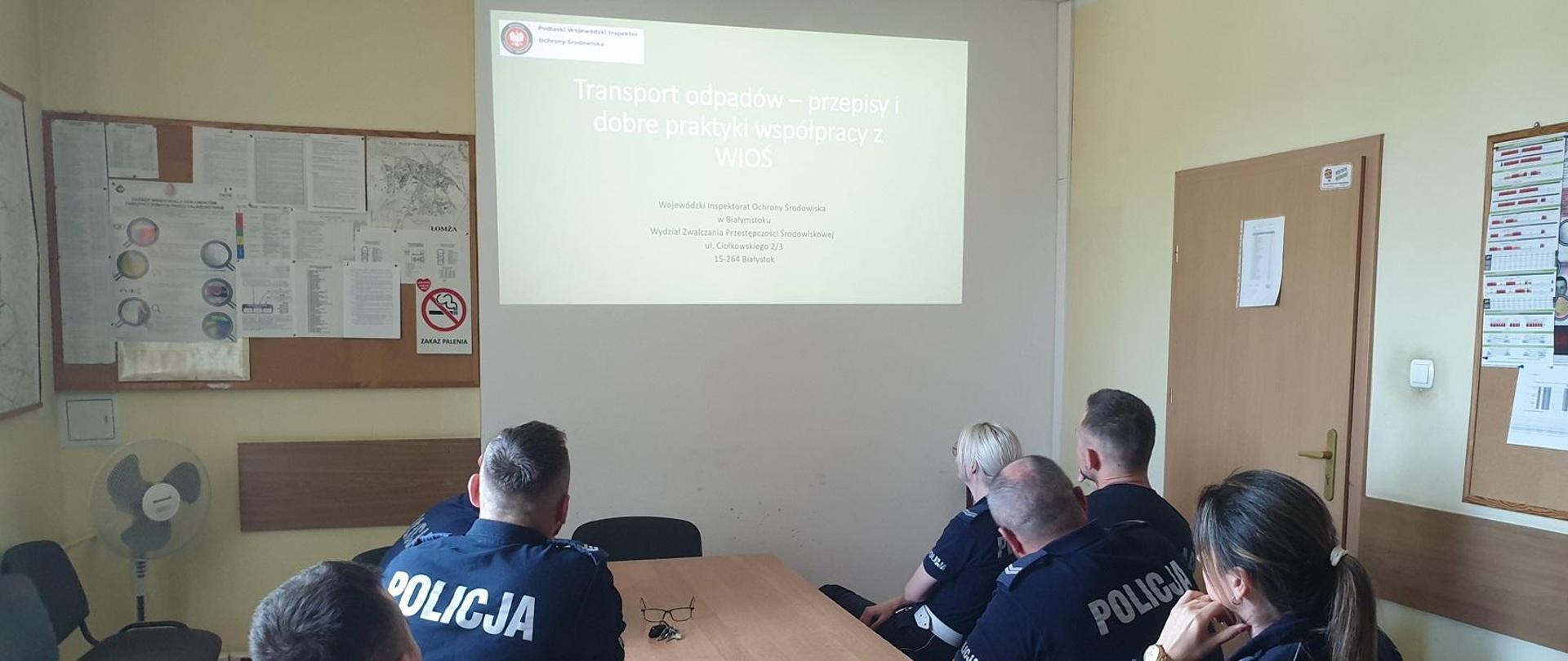 Grupa policjantów znajdująca się w pomieszczeniu ogląda wyświetlaną prezentację. Osoby są obróceni plecami.
