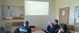 Grupa policjantów znajdująca się w pomieszczeniu ogląda wyświetlaną prezentację. Osoby są obróceni plecami.