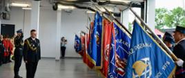 Przegląd pododdziałów – na pierwszym tle poczty sztandarowe prezentujące sztandary. W tle salutujący oficerowie PSP.