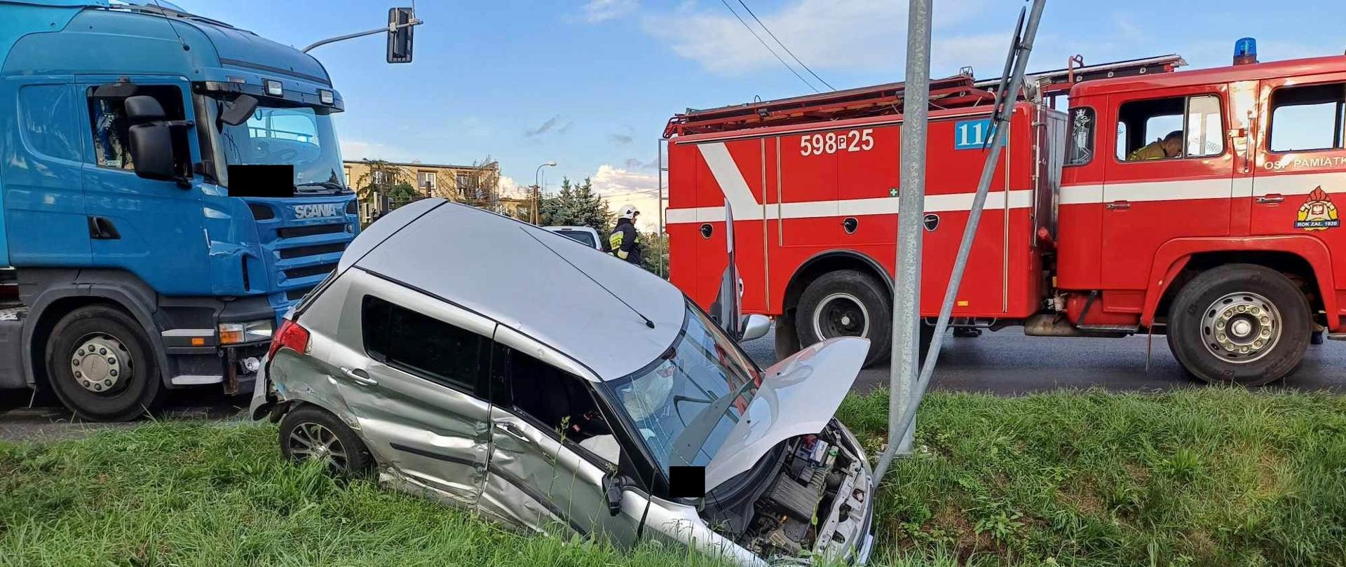 Po lewej niebieski samochód ciężarowy i srebrny samochód osobowy w rowie, po prawej samochód strażacki