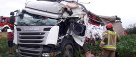 Rozbity samochód ciężarowy, przy nim strażak PSP. W tle samochód pożarniczy.