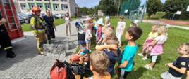 Na zdjęciu strażacy prezentują dzieciom ubranie specjalne do działań gaśniczych
