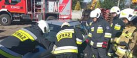 Zdjęcie przedstawia strażaków podczas rozcinania elementów karoserii samochodu z użyciem narzędzi hydraulicznych.
