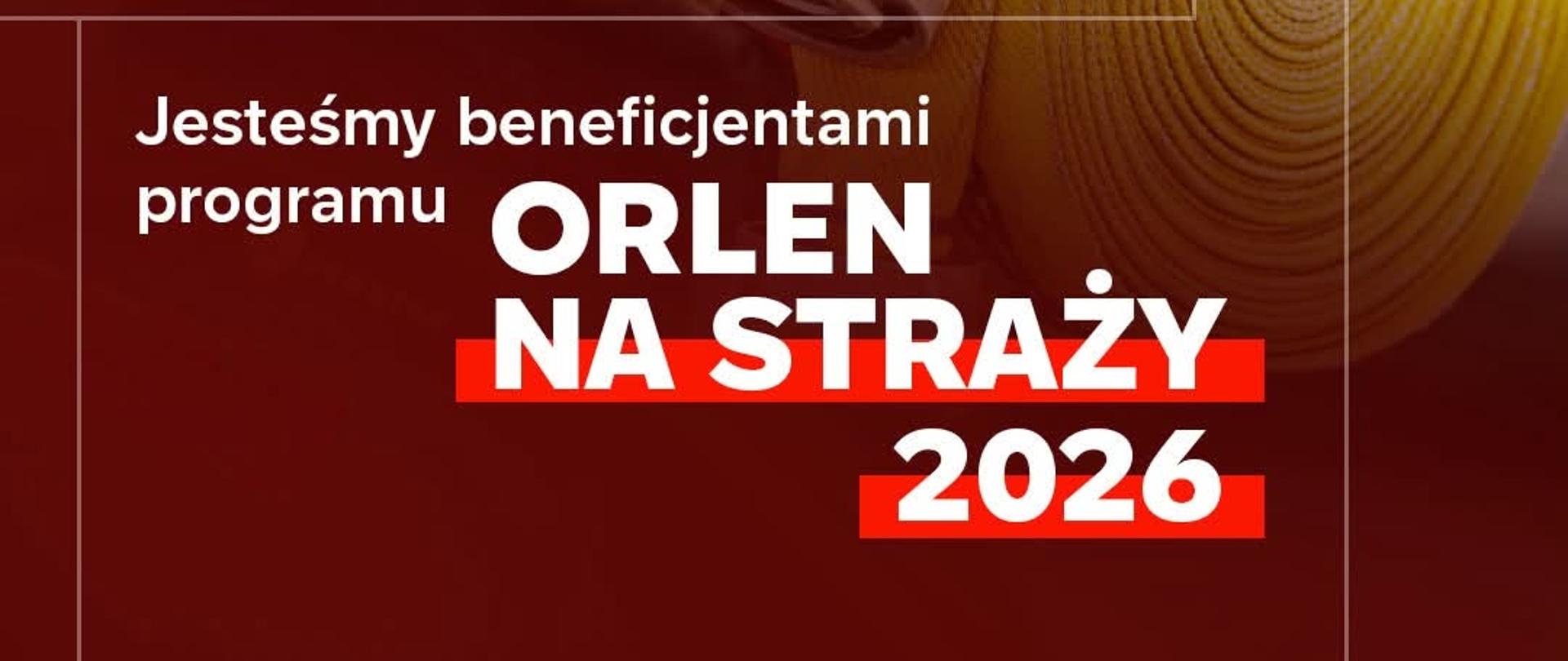 Grafika promocyjna w pionowym formacie. Główny kadr przedstawia zbliżenie na postać strażaka ubranego w ciemne ubranie specjalne z odblaskowymi elementami. Strażak trzyma w dłoni w rękawicy bojowej zwinięty w krąg, żółty wąż tłoczny ze złączem. W prawym górnym rogu widoczne jest logo „ORLEN FUNDACJA”. Dolną część grafiki zajmują białe napisy na bordowym tle: „Pierwsi tam, gdzie potrzebna jest pomoc”, a poniżej: „Jesteśmy beneficjentami programu ORLEN NA STRAŻY 2026”, gdzie nazwa programu oraz rok wyróżnione są pogrubionym krojem pisma i czerwonym tłem