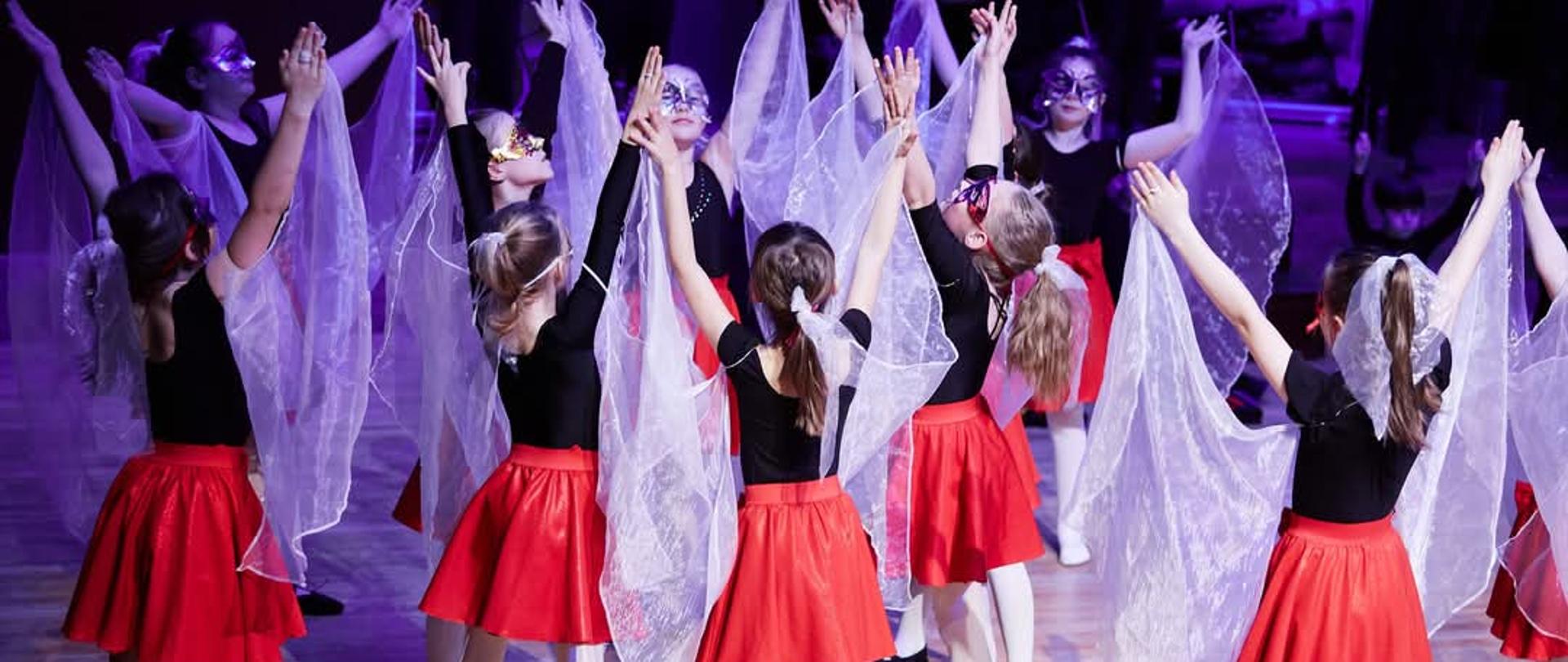 Tańczące dzieci ubrane w spódnice czerwone z kawałkami materiału wznoszą ręce ku górze