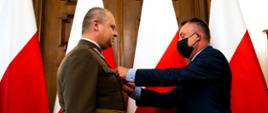 Wicewojewoda łódzki wręcza odznaczenie państwowe na tle biało-czerwonych flag 