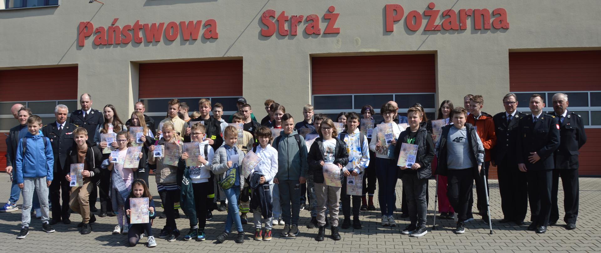 Eliminacje powiatowe OTWP. Plac manewrowy przed Komendą Powiatową PSP w Rawiczu. Na tle bram wraz kierownictwem komendy oraz zarządu oddziału powiatowego ZOSP RP, do wspólnego zdjęcia pozują wszyscy uczestnicy eliminacji. Trzymają w rękach dyplomy.