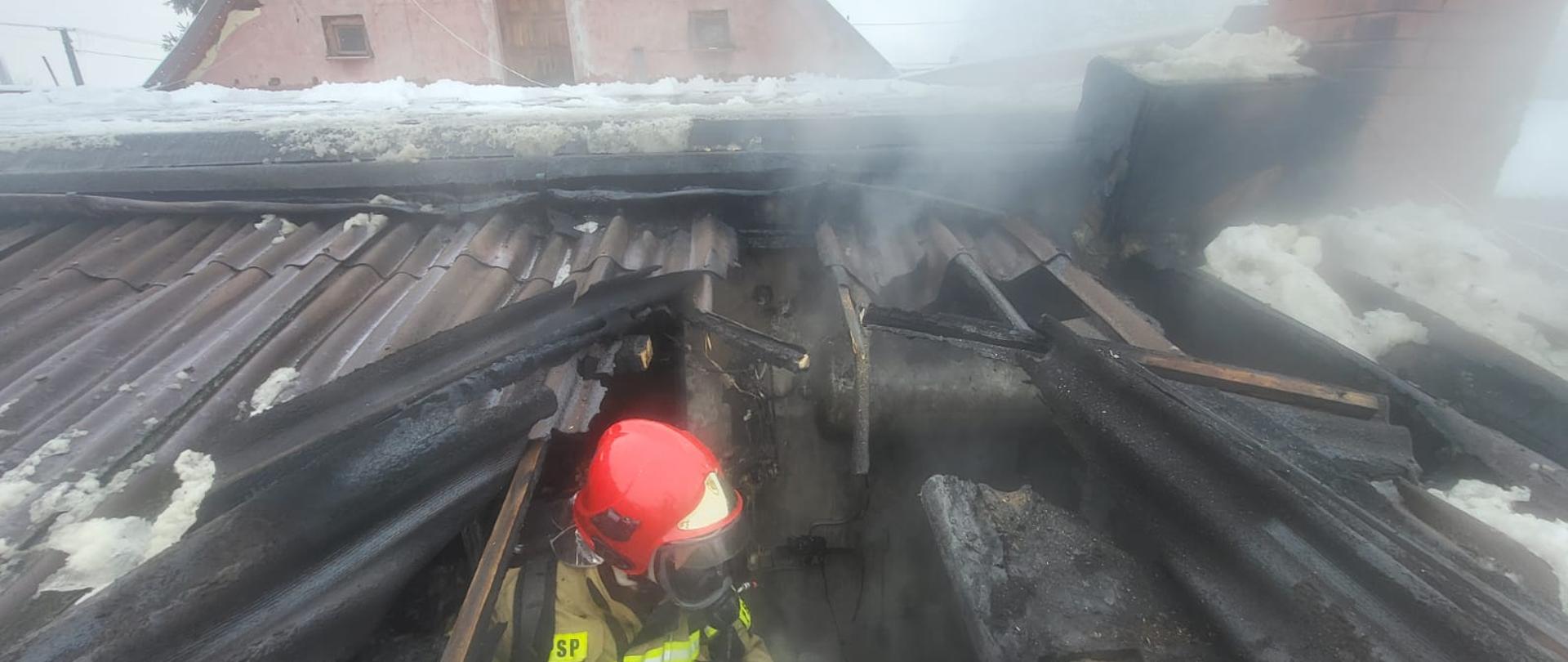 Uszkodzony dach pomieszczenia kotłowni, widać strażaka