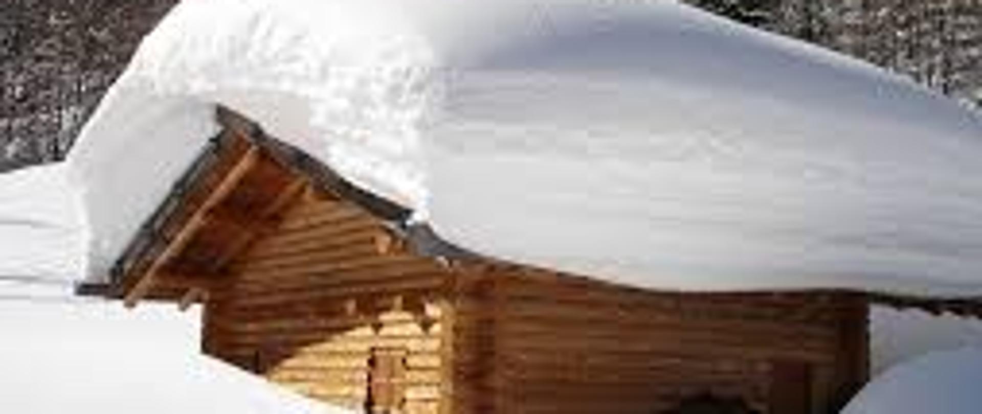 Na zdjęciu znajduje się drewniany domek przysypany dużą ilością śniegu,