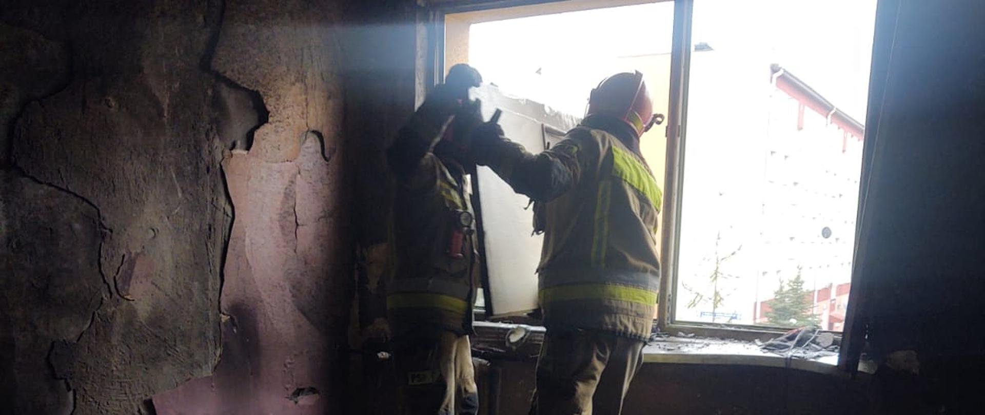 Strażacy wyrzucają spalone elementy przez okno.