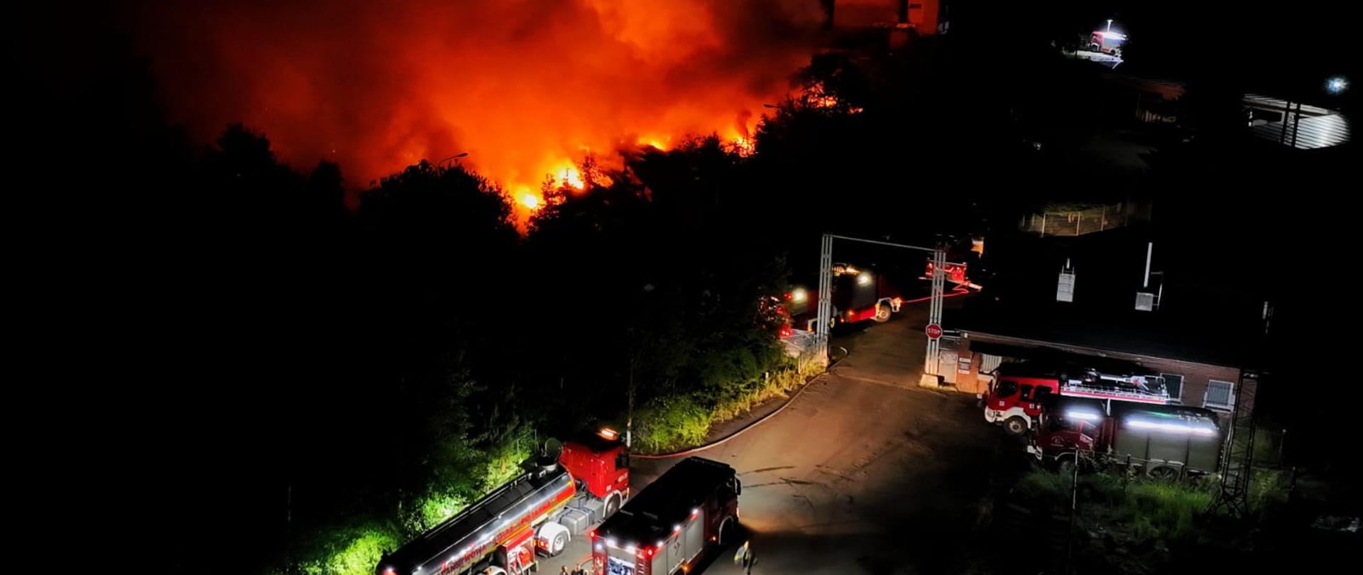 pora nocna, ujęcie z drona miejsca pożaru, widoczne płomienie oraz oświetlone pojazdy strażackie